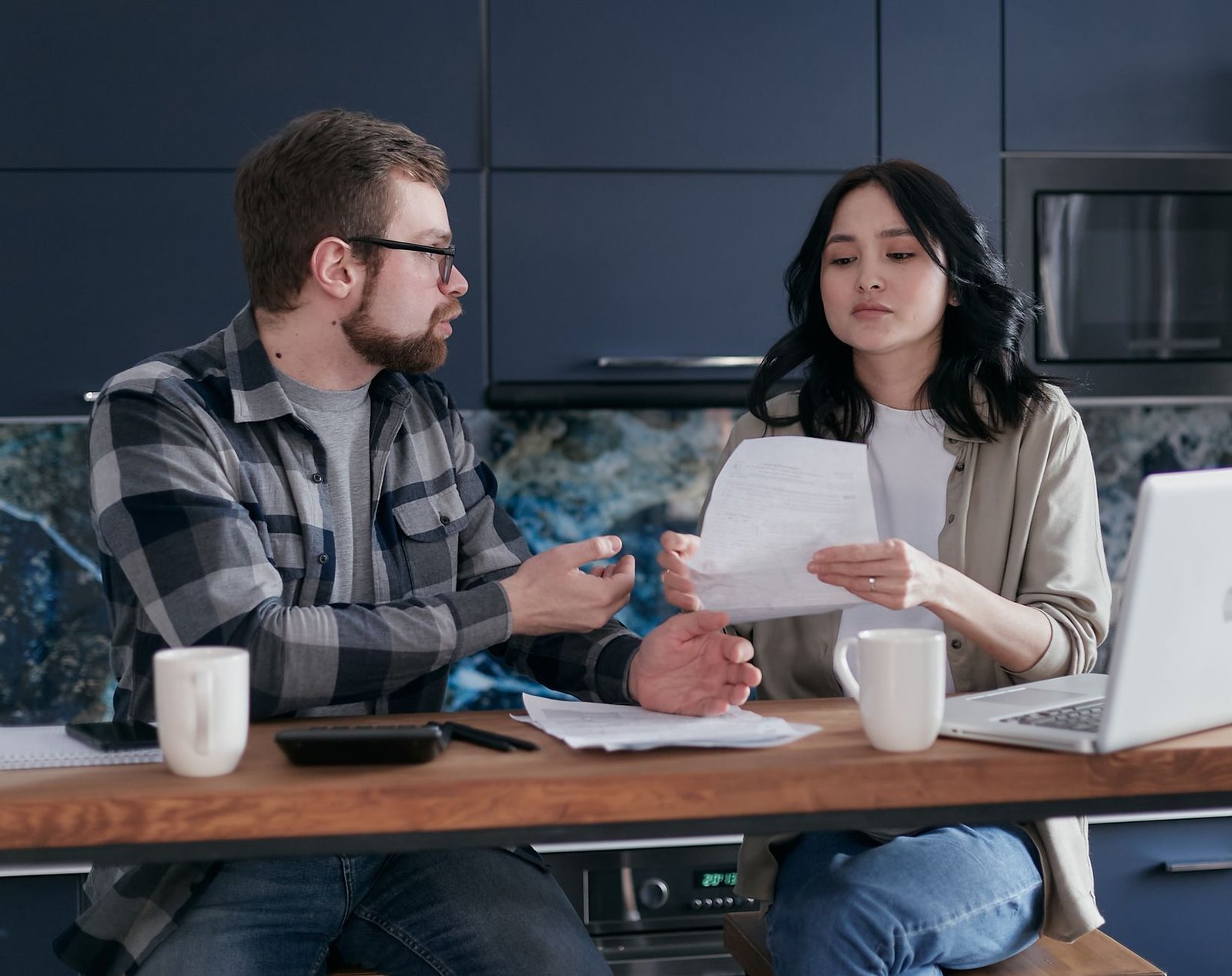 Person reading an explanation of benefits statement beside a medical bill and laptop at a kitchen table